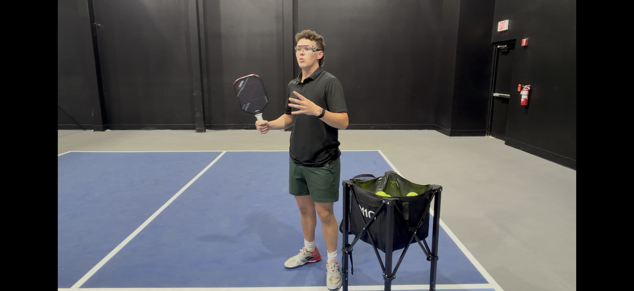 Coach Ryan explaining a drill next to a ball hopper on court